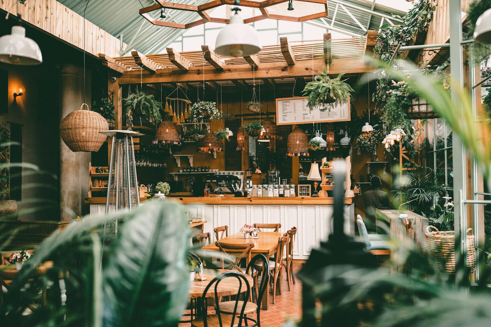 A cafe full of plants, with rattan lamps over the counter